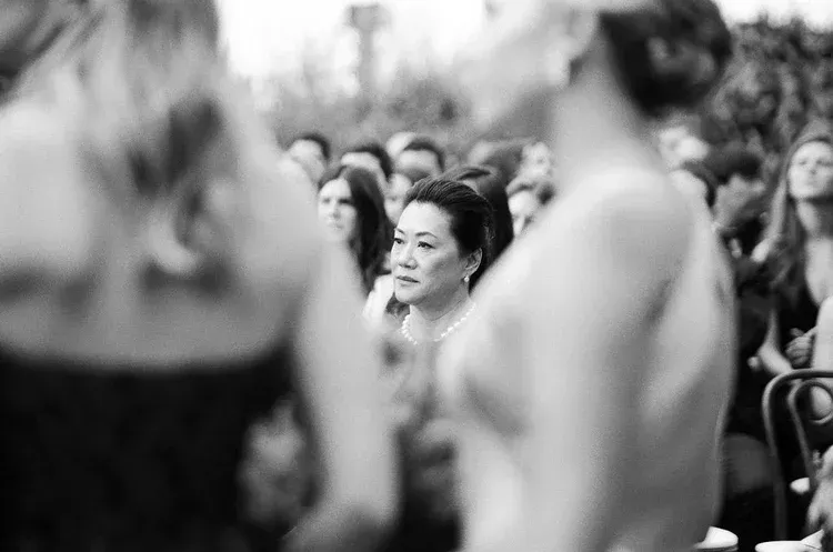 Woman seated among a blurred crowd, looking forward in a black-and-white audience scene
