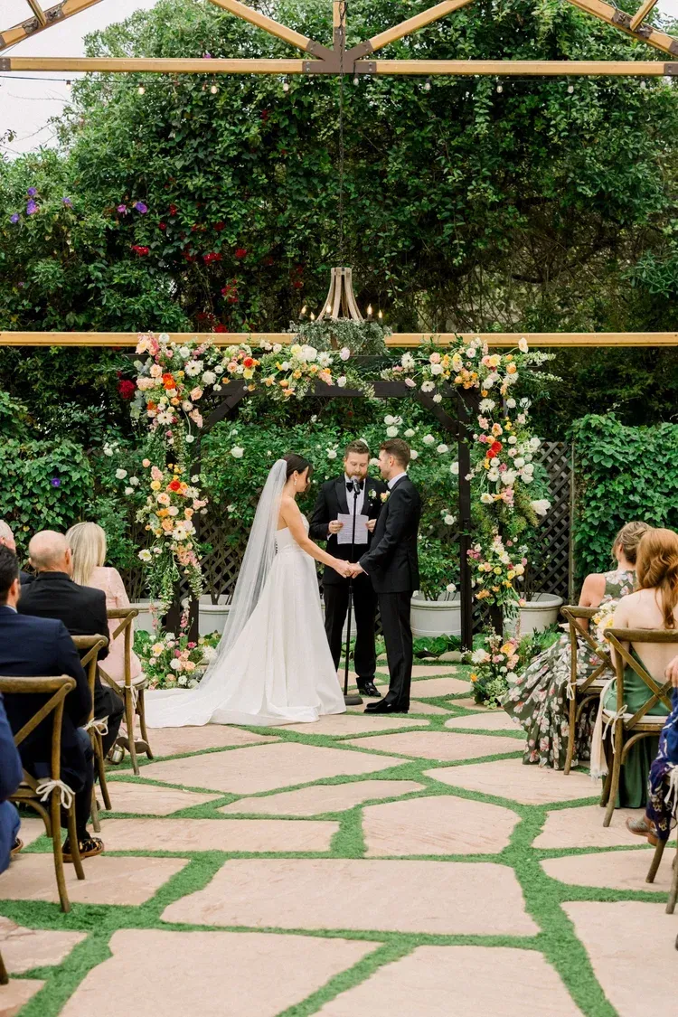 Bride and groom exchanging vows under a floral arch in an outdoor garden ceremony