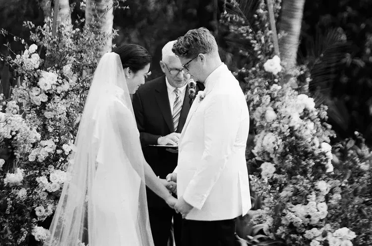 Wedding couple exchanging vows under a floral arch in black-and-white.