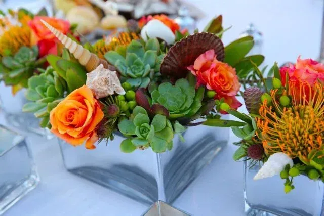 Succulent and orange floral arrangements in mirrored square vases on a white table