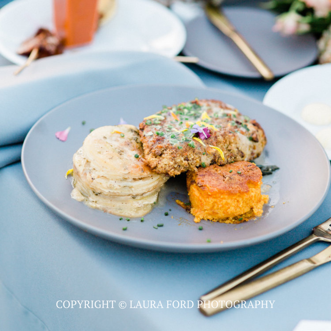 Plated gourmet meal with mashed potatoes, fried chicken, and a baked side on a blue tablecloth