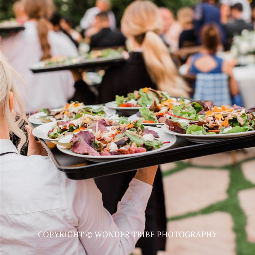 Server carrying trays of salads and appetizers at an outdoor event