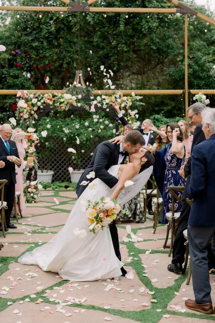 Bride and groom kissing at outdoor wedding ceremony under floral arch