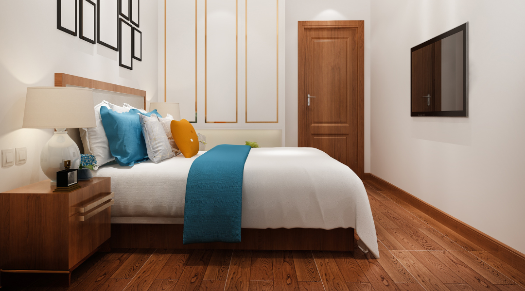 Modern bedroom with white bed, blue throw, wooden floor, bedside table, and wall-mounted TV