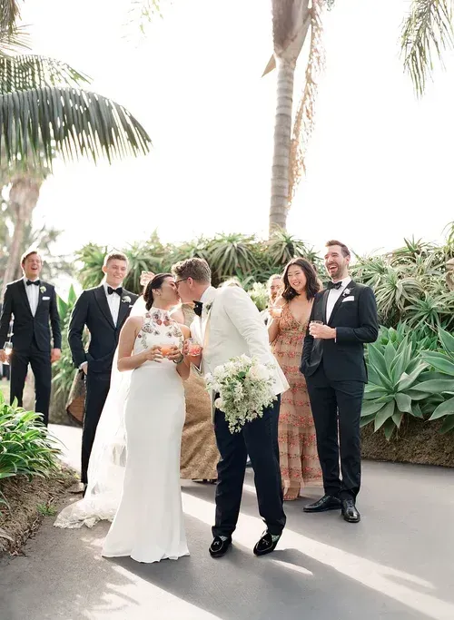 Wedding couple kissing in a tropical garden, with guests standing nearby.