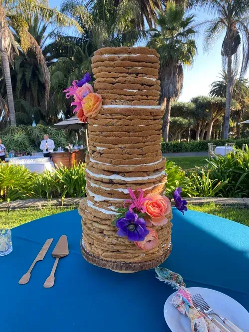 Tall stacked dessert tower with flowers on a blue table outdoors by a pool and palm trees