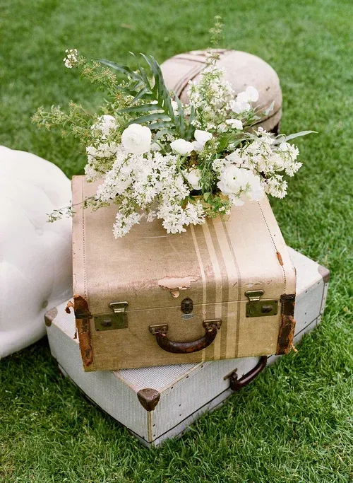 Vintage suitcases with white flowers arranged on grass for an outdoor display