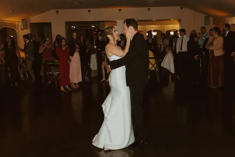 Couple slow dancing at a formal indoor reception, bride in a white gown and partner in a black suit