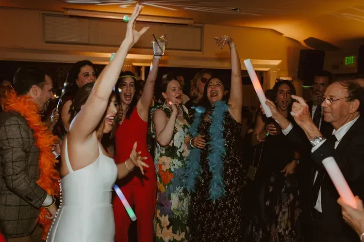People cheering and dancing at a lively indoor party, arms raised with glowing sticks