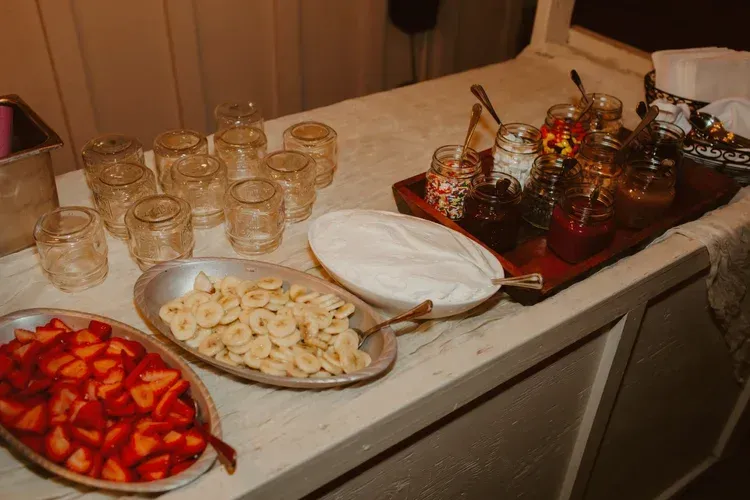 Buffet table with jars of drinks and trays of sliced strawberries, bananas, and plates ready to serve