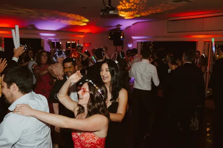 People dancing at a crowded party with colorful lights and a disco ball overhead