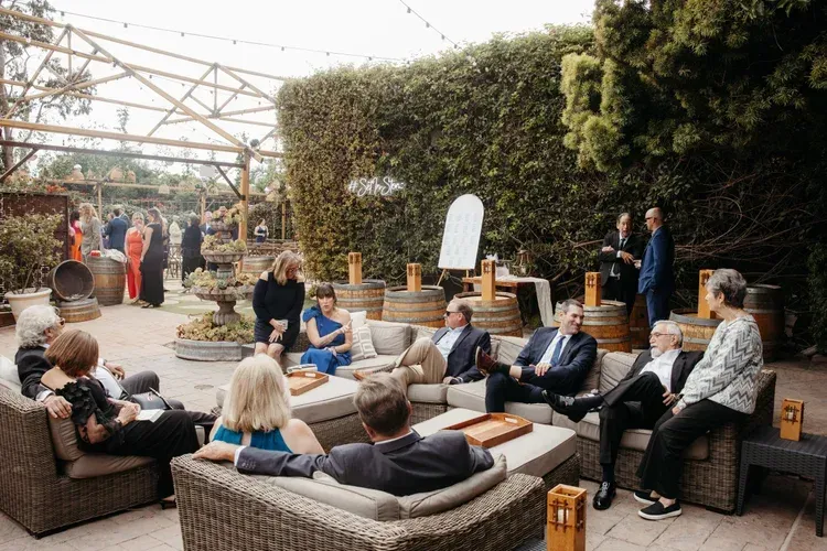 People relaxing on wicker seating in an outdoor garden lounge under a greenhouse canopy