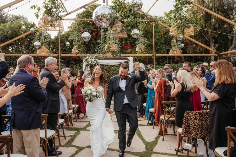 Wedding couple walking down the aisle under a greenhouse canopy, guests clapping around them