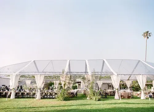 White event tent with draped sides on a grassy lawn under a bright sky