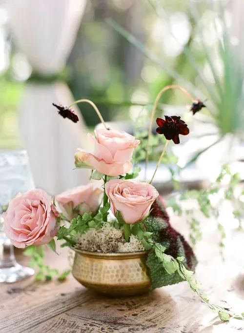 Pink roses and dark flowers in a gold vase on a rustic table in soft natural light