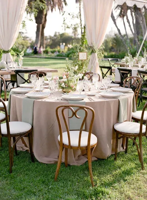 Round banquet table set under draped canopy in a garden, with white and gold chairs and place settings