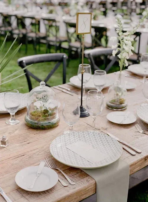 Elegant outdoor table setting with white dishes, glass cloches, and candles on a wooden table