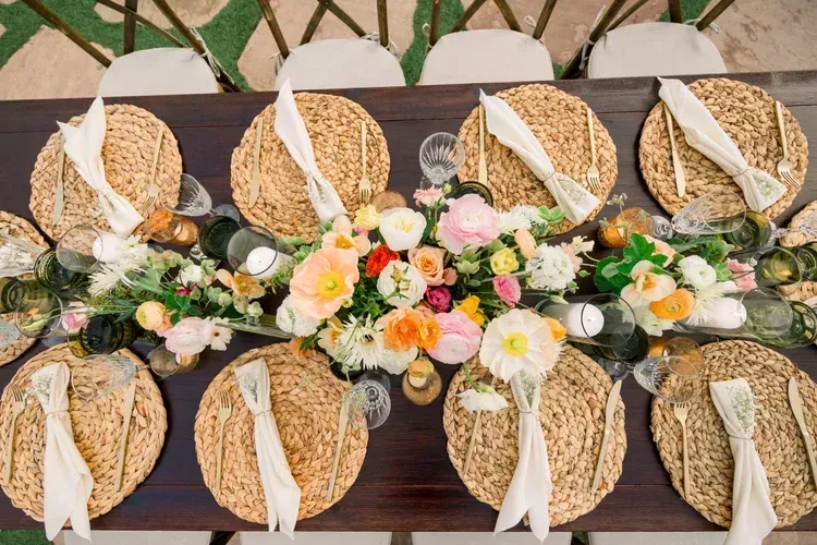 Outdoor table set with round woven placemats and white napkins, decorated with pastel floral centerpieces.