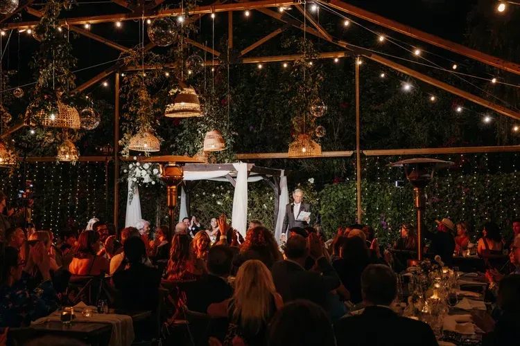 String-lit outdoor dinner event with guests seated at tables under a canopy, warmly lit at night
