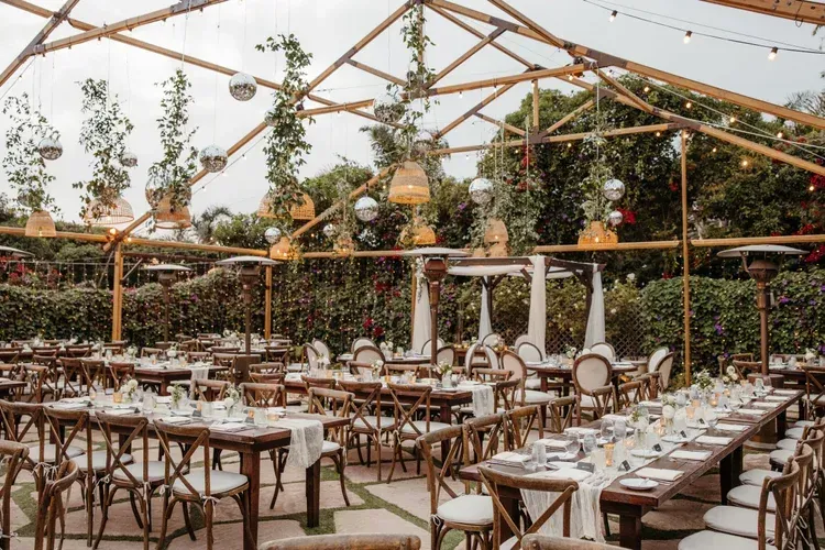Elegant outdoor dining tent with white tablecloth tables, wooden chairs, and greenery overhead