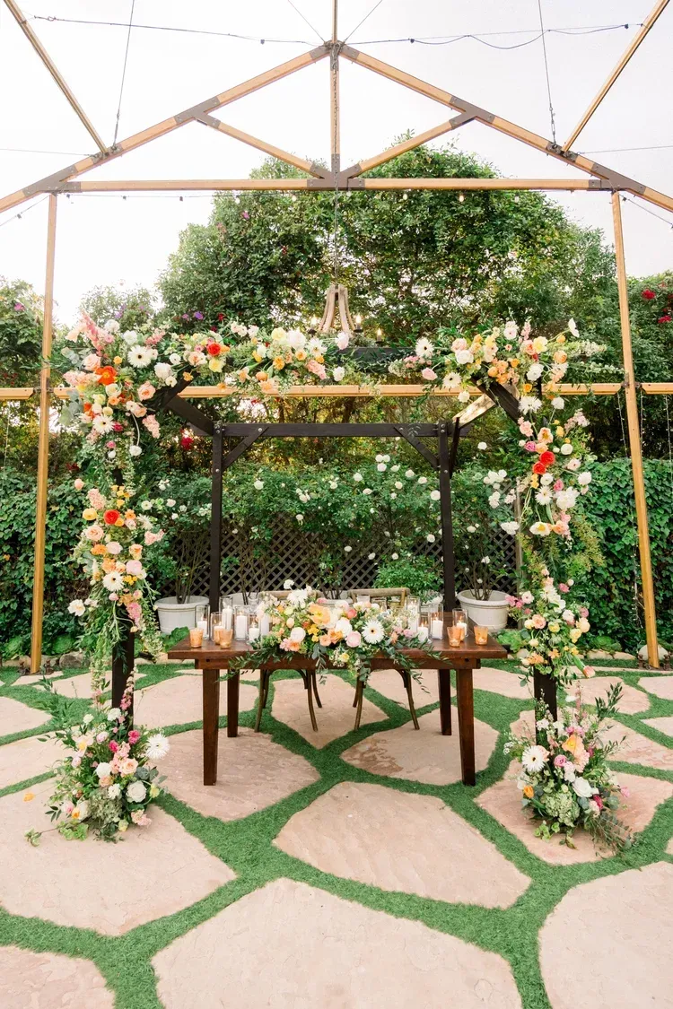 Flower-decorated wedding arch with tables in a garden setting under a white canopy