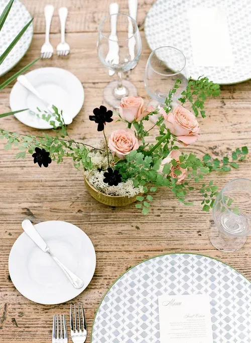 Elegant rustic table setting with white plates, silverware, glassware, and a floral centerpiece on wood.
