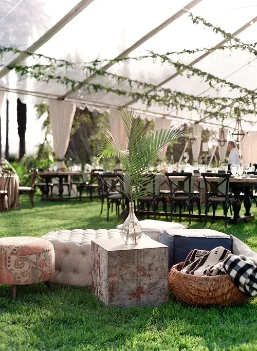 Elegant outdoor tented event with tables, draped curtains, and grass seating in the foreground