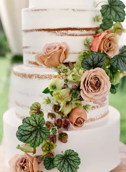 White tiered cake with peach roses, green leaves, and gold trim accents