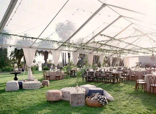 Outdoor tent reception with green lawn, string lights, and rustic tables and seating