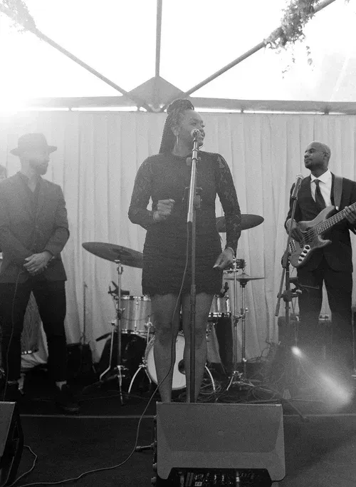 Band performs on an outdoor stage with microphones, drums, and guitar under a tent canopy.