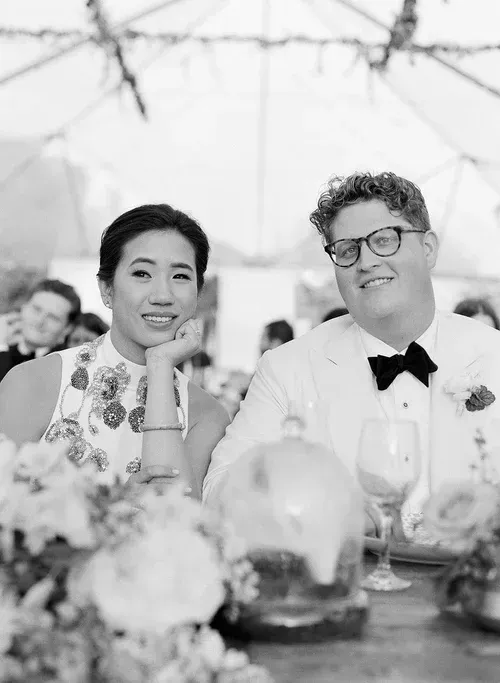 Two people seated at a decorated table, smiling at an outdoor event under a tent.