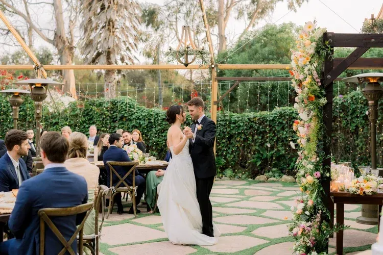 Bride and groom share a dance under a floral arch at an outdoor wedding reception