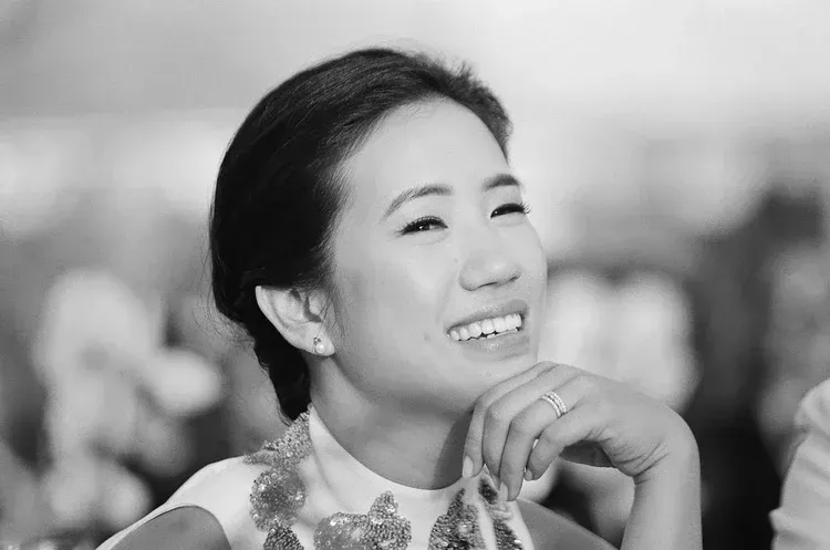 Smiling person in a patterned top resting their chin on their hand, in a softly blurred background.