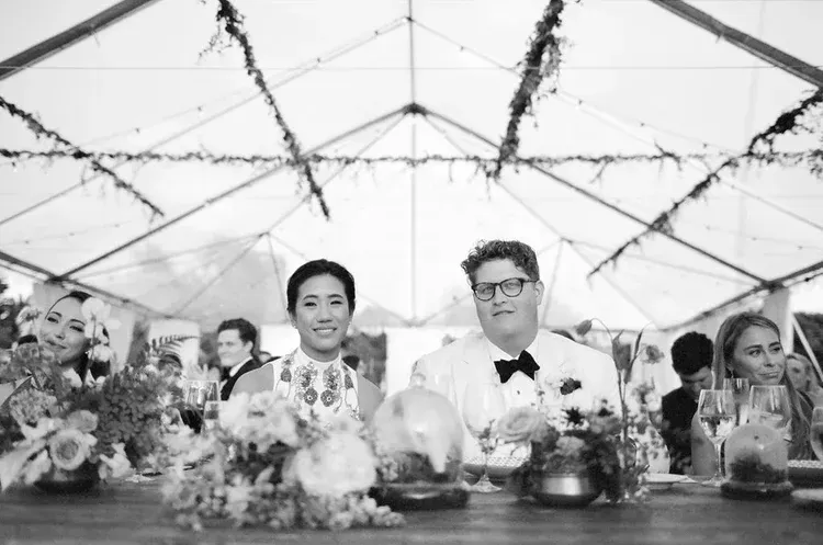 Guests seated at a decorated banquet table inside a tent, smiling toward the camera
