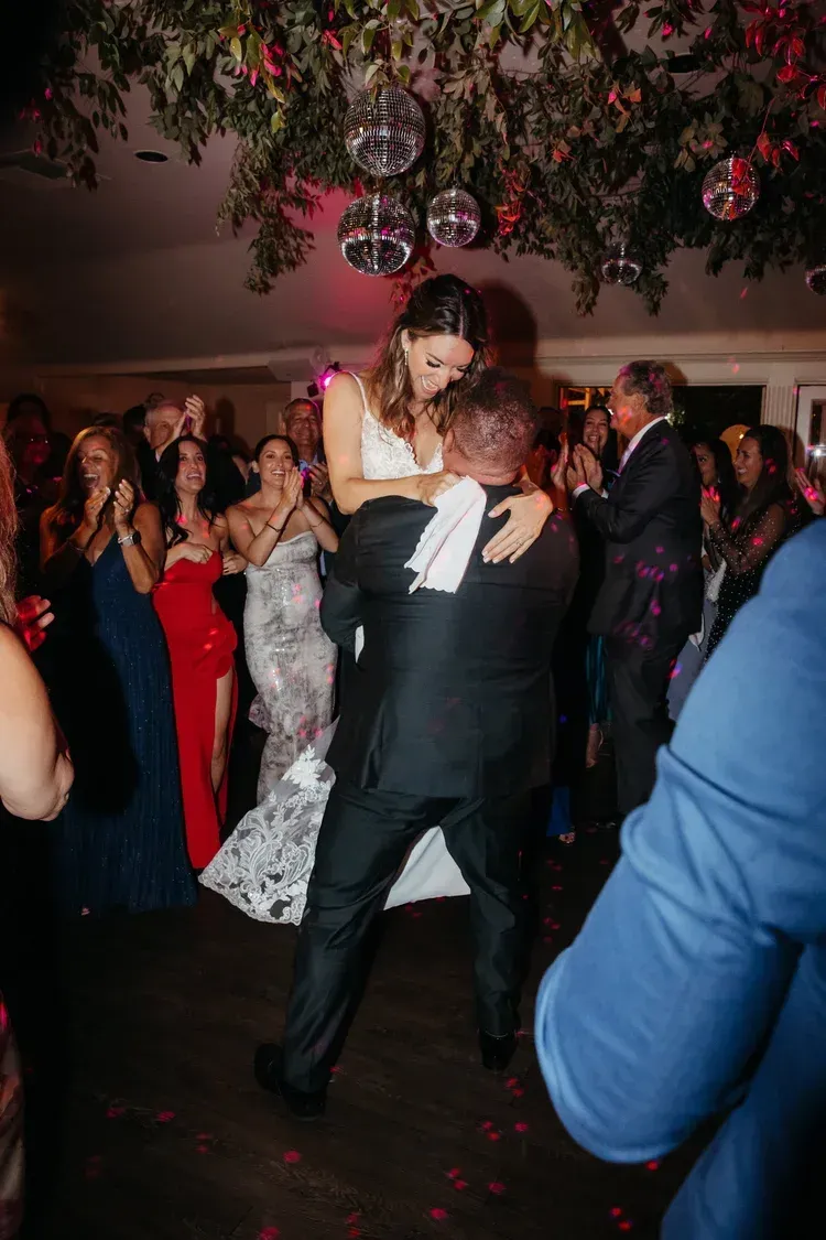 Couple dancing at a formal reception, with guests watching under floral ceiling decor.