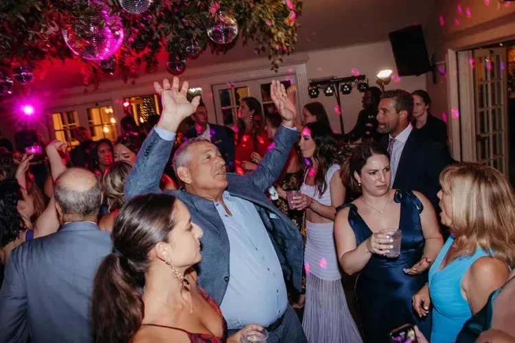 Crowded dance floor at a lively party with colorful lights and people raising their hands