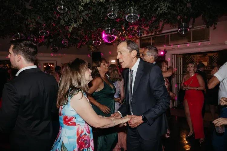 Couple dancing at a crowded indoor party with pink lighting and hanging decorations