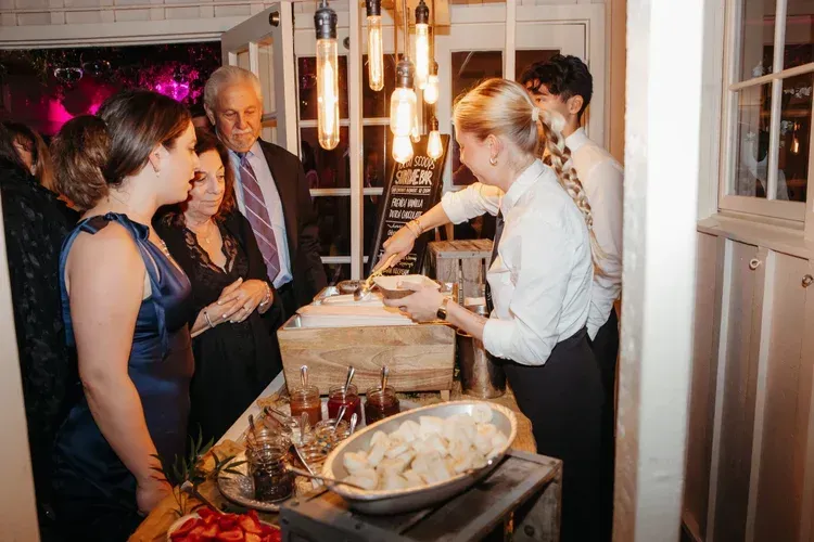 Guests at a buffet table in a warmly lit room, serving food and drinks at a social event