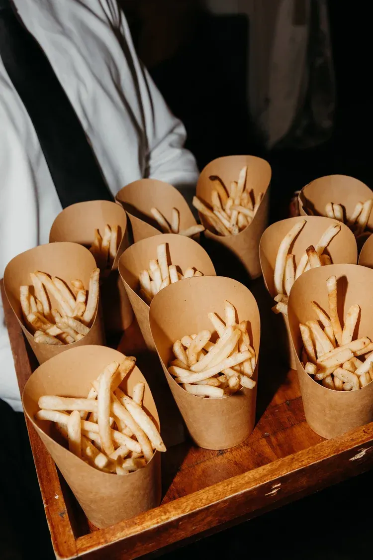Wooden tray of paper cups filled with French fries, held by a person in a white shirt
