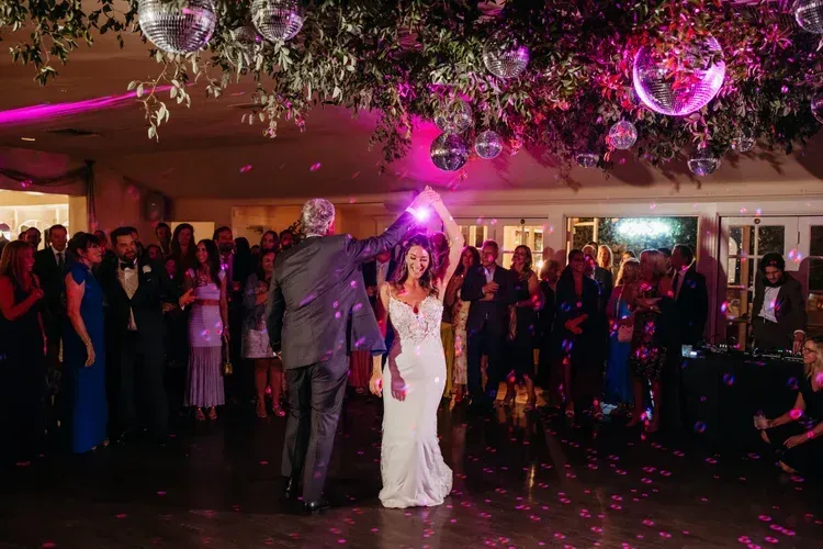 Couple dancing at a candlelit reception with guests watching under pink and silver disco balls