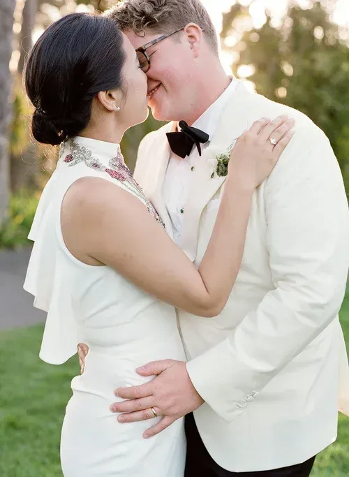 Couple in white formalwear embracing and smiling outdoors at sunset