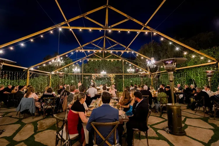 Outdoor evening dining under a string-lit canopy with guests seated at tables in a garden patio