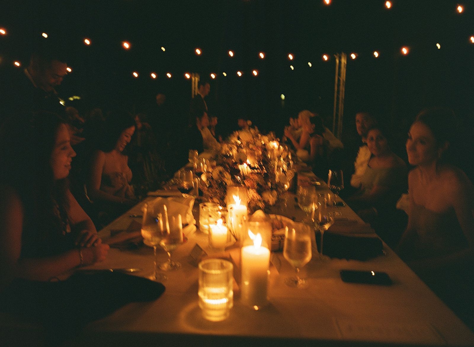 People seated around a candlelit dinner table at night outdoors