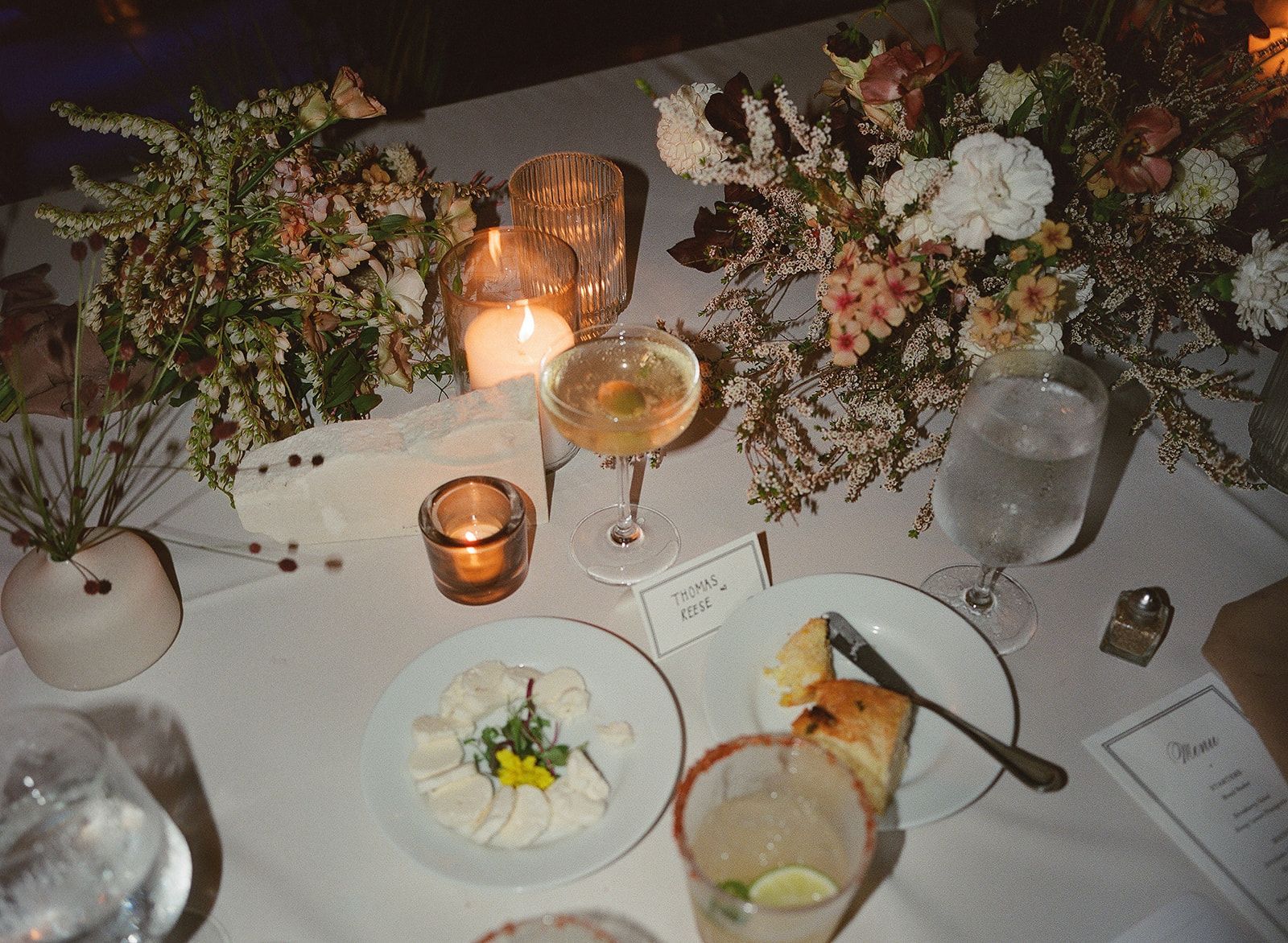 Elegant dinner table with candles, floral centerpiece, wine glasses, and plated desserts and bread