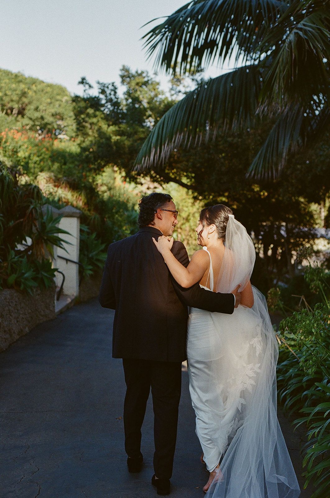 Bride and groom walking hand in hand on a sunlit garden path