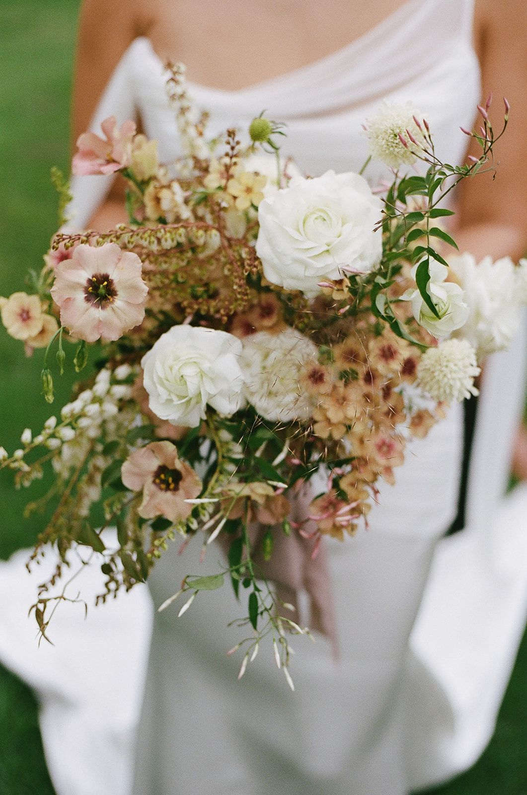 Bride holding a white and blush wildflower bouquet with greenery