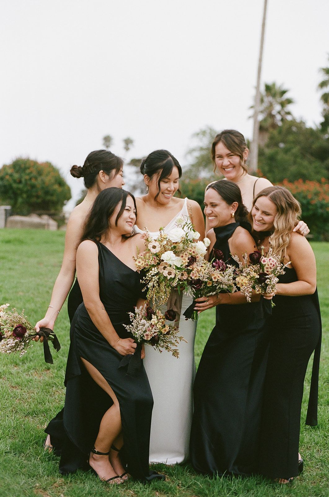 Wedding party posing outdoors in black dresses and bouquets around a bride in white