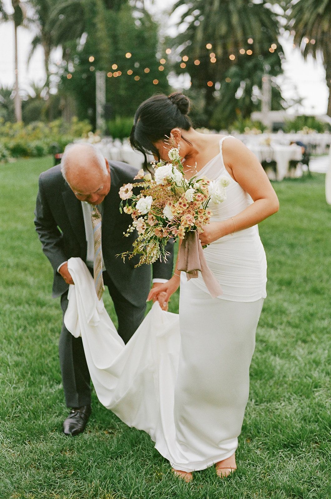 Bride and groom adjusting her white wedding dress on a grassy lawn outdoors