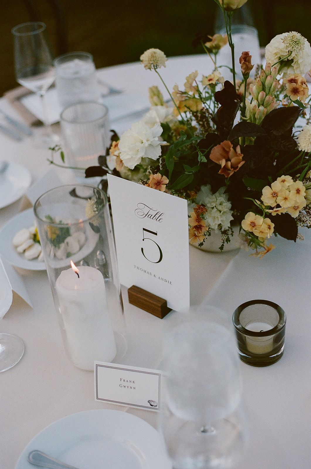 Elegant white table setting with floral centerpiece, candles, and a small table number card