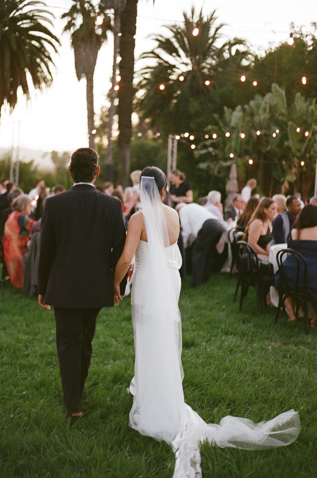 Bride and groom walking through a garden wedding reception at sunset